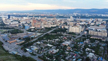 Fototapeta premium Aerial panorama revealing krasnoyarsk cityscape, spanning yenisei river, urban neighborhoods, industrial sectors, transportation networks beneath overcast skies