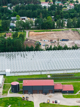 Aerial view of a waste management service facility with industrial buildings, a large greenhouse, and surrounding green landscape in Rumbula, Ropazi Municipality, Latvia.