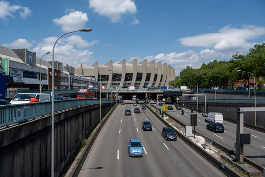 Busy traffic on the Boulevard Peripherique ring road passing by the iconic Parc des Princes stadium in Paris, France, under a clear blue sky with white clouds on a sunny day