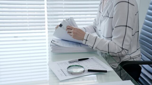 Professional woman categorizing important business documents and financial statements on an office desk. Managing a stack of files during a detailed audit