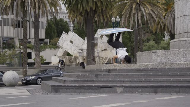 Man Performing Headstand on Plaza Steps And Balancing  Board - Wide Shot