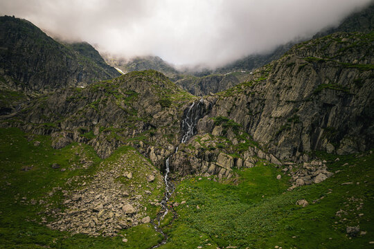 Aerial view of Negoiu Peak in the Fagaras Mountains, featuring a cascading waterfall flowing down rugged rocky slopes with lush green vegetation in Porumbacu de Jos, Sibiu, Romania.