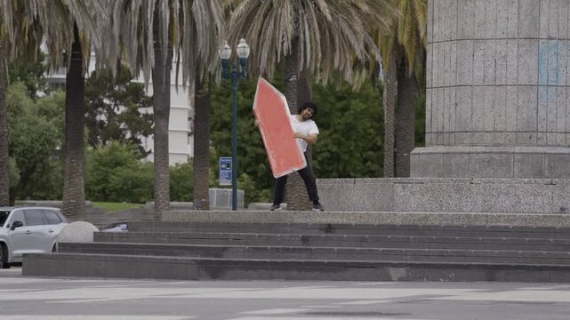 Man Spinning Blue Cross Board on Plaza Steps As Pedestrians Pass By - Wide Shot