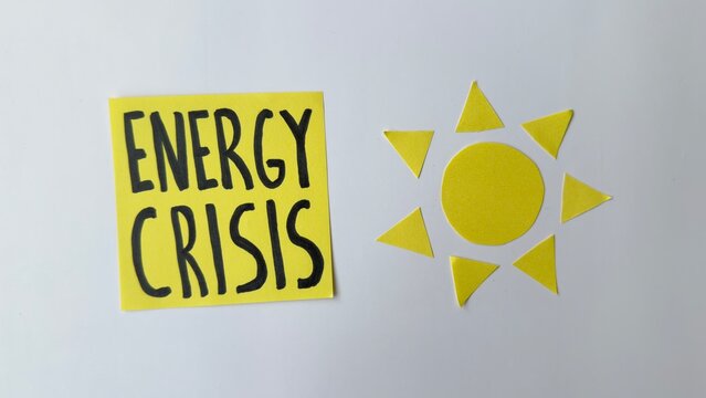 Yellow sticky note says 'Energy Crisis'. Beside it, a yellow paper sun cutout. Minimalist design with white background. Suggests environmental or economic theme. Useful for news, reports