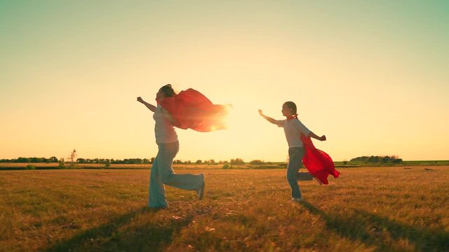 Happy children playing superheroes, running sunny field in red capes. Childhood games dreams. Teenage girls dream becoming superheroes. Young girls in red capes. Children games outdoors. Slow motion.
