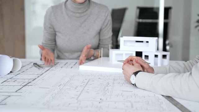Architectural team analyzing building plans and a white scale model, discussing design concepts and construction details during a professional meeting in an office environment, close up