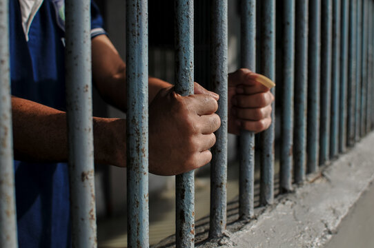 prisoner's hands behind bars with black background