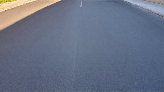 An empty asphalt road extends into the horizon, its clean lines and smooth surface inviting contemplation of endless journeys, new beginnings, and the quiet freedom of the open path