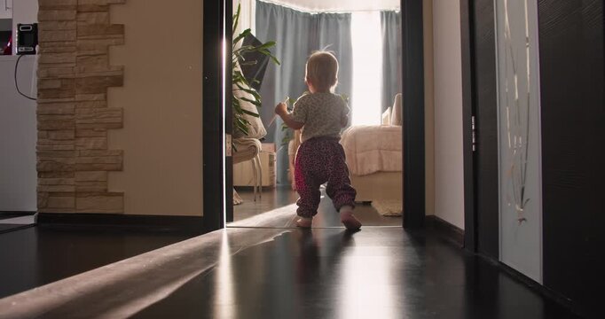 Small child walking through hallway while learning balance. First steps milestone in everyday home life