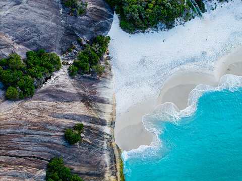 Aerial view of Misery Beach featuring white sand, turquoise ocean waves, and rugged rocky cliffs with coastal vegetation in Torndirrup, Western Australia, Australia.
