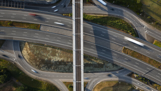 Aerial view of a highway intersection with a railway line crossing over the roads, featuring moving vehicles and green surroundings in Portugal.