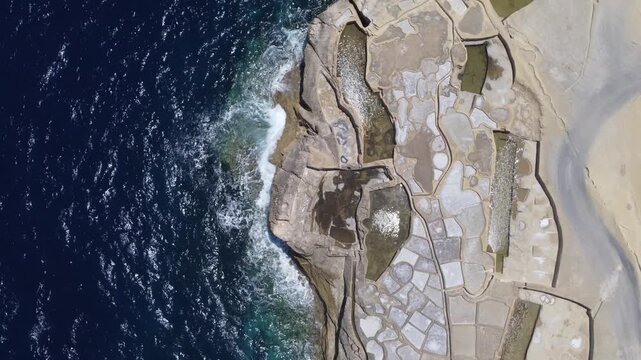 Xwejni s centuries-old salt pans unfold along the rugged coast of Zebbug, Gozo, geometric pools and vivid Mediterranean blues in a sweeping summer Aerial view. High quality 4k footage