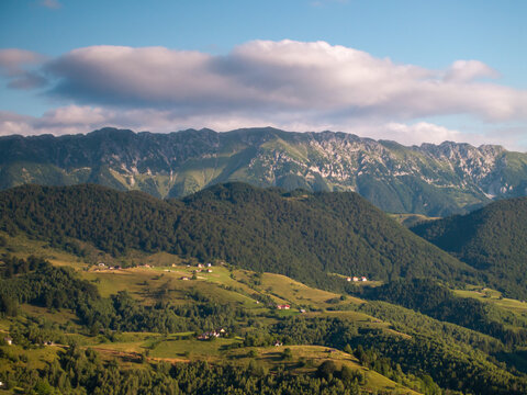 Aerial view of the Piatra Craiului Mountains with lush green forests, rolling hills, and scattered rural houses in Zarnesti, Brasov, Romania.