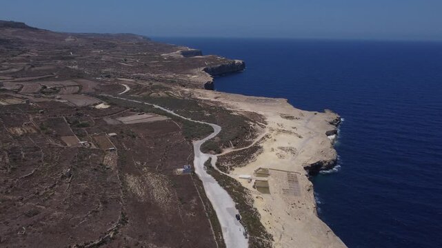 Xwejni s centuries-old salt pans unfold along the rugged coast of Zebbug, Gozo, geometric pools and vivid Mediterranean blues in a sweeping summer Aerial view. High quality 4k footage