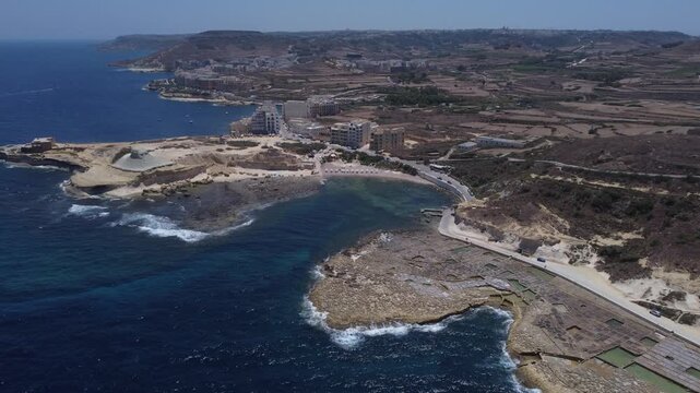 Xwejni s centuries-old salt pans unfold along the rugged coast of Zebbug, Gozo, geometric pools and vivid Mediterranean blues in a sweeping summer Aerial view. High quality 4k footage