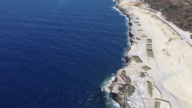 Xwejni s centuries-old salt pans unfold along the rugged coast of Zebbug, Gozo, geometric pools and vivid Mediterranean blues in a sweeping summer Aerial view. High quality 4k footage