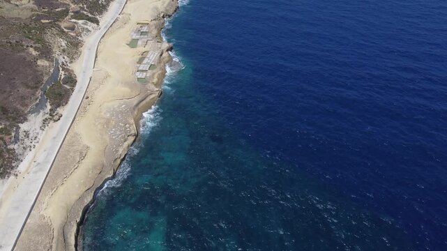 Xwejni s centuries-old salt pans unfold along the rugged coast of Zebbug, Gozo, geometric pools and vivid Mediterranean blues in a sweeping summer Aerial view. High quality 4k footage