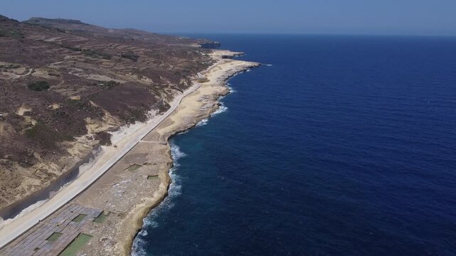 Xwejni s centuries-old salt pans unfold along the rugged coast of Zebbug, Gozo, geometric pools and vivid Mediterranean blues in a sweeping summer Aerial view. High quality 4k footage