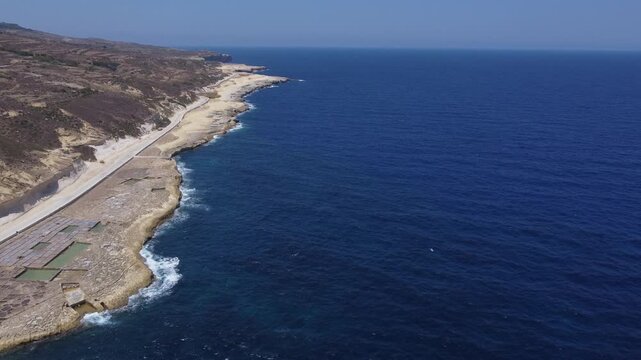Xwejni s centuries-old salt pans unfold along the rugged coast of Zebbug, Gozo, geometric pools and vivid Mediterranean blues in a sweeping summer Aerial view. High quality 4k footage