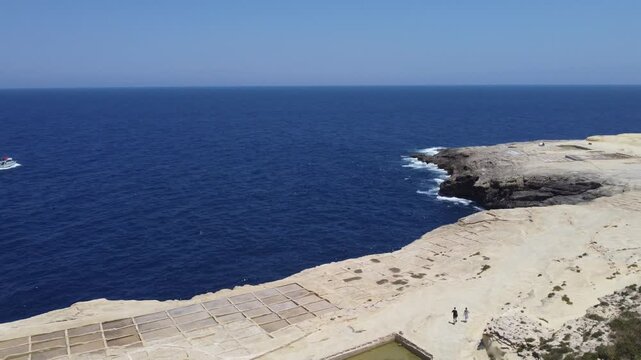 Xwejni s centuries-old salt pans unfold along the rugged coast of Zebbug, Gozo, geometric pools and vivid Mediterranean blues in a sweeping summer Aerial view. High quality 4k footage