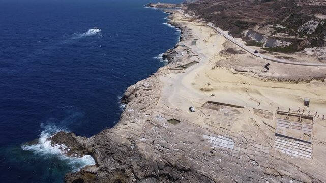 Xwejni s centuries-old salt pans unfold along the rugged coast of Zebbug, Gozo, geometric pools and vivid Mediterranean blues in a sweeping summer Aerial view. High quality 4k footage
