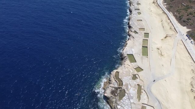 Xwejni s centuries-old salt pans unfold along the rugged coast of Zebbug, Gozo, geometric pools and vivid Mediterranean blues in a sweeping summer Aerial view. High quality 4k footage