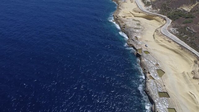 Xwejni s centuries-old salt pans unfold along the rugged coast of Zebbug, Gozo, geometric pools and vivid Mediterranean blues in a sweeping summer Aerial view. High quality 4k footage