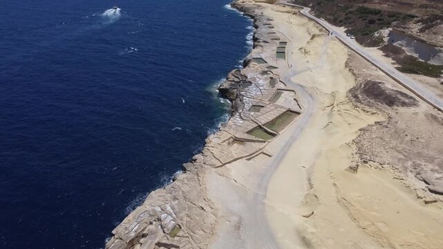 Xwejni s centuries-old salt pans unfold along the rugged coast of Zebbug, Gozo, geometric pools and vivid Mediterranean blues in a sweeping summer Aerial view. High quality 4k footage