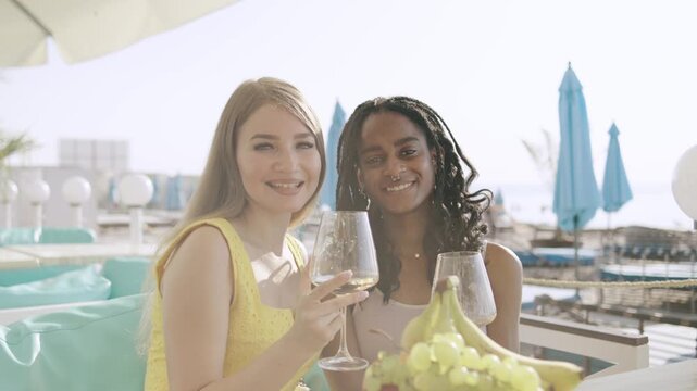Two multiracial friends enjoy drinks and fruit at a beachside restaurant during summer vacation in the Caribbean