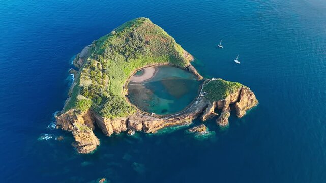 Volcanic islet with circular inner lagoon, rocky shoreline and deep blue ocean backdrop, Sao Miguel Azores, aerial view