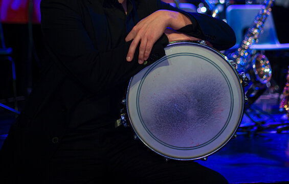 Close-up details of jazz instruments and musicians performing on stage under dramatic blue and purple concert lighting, featuring saxophone, piano, drumsticks and live music atmosphere.