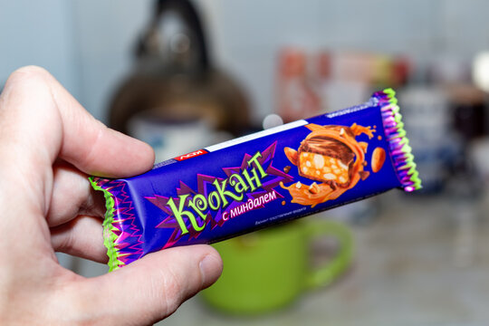 Hand holding a purple wrapped almond candy bar with nuts and caramel