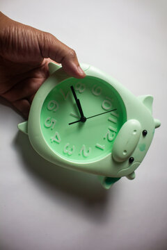 Hand holding a cute pastel green animal-shaped analog alarm clock on a white background, representing time management and morning routine.