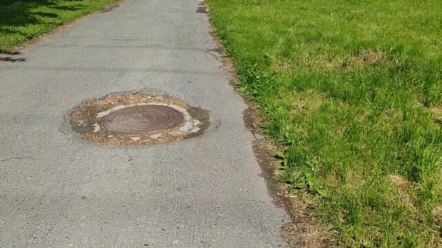 Paved path with manhole cover surrounded by green grass