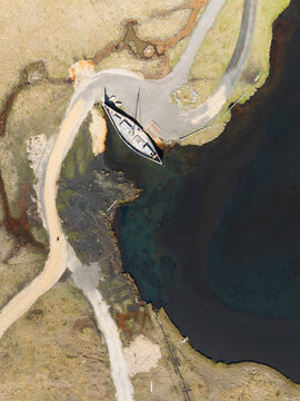 Aerial view of the Viking village film set at Stokksnes, featuring a wooden ship replica docked in a dark coastal inlet, surrounded by rugged terrain and gravel paths in Iceland.