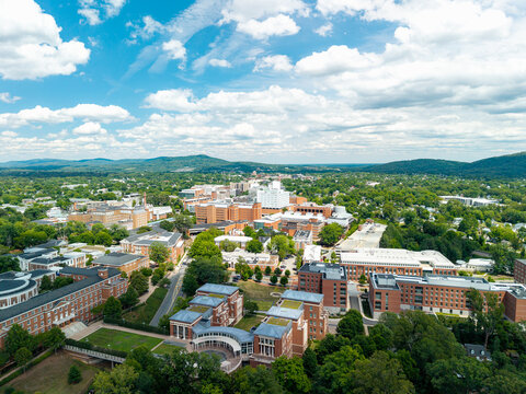 Charlottesville, Virginia, wide aerial drone view looking over the expansive University of Virginia campus and medical center complex, stretching toward rolling green hills under a bright sky 