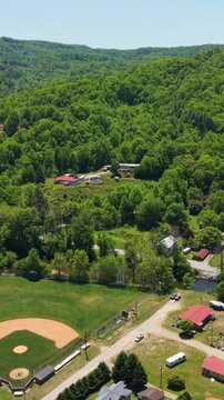 Vertical screen. Aerial perspective of Rosman, North Carolina, featuring a baseball field, lush green hills, and nearby residential structures in a scenic setting