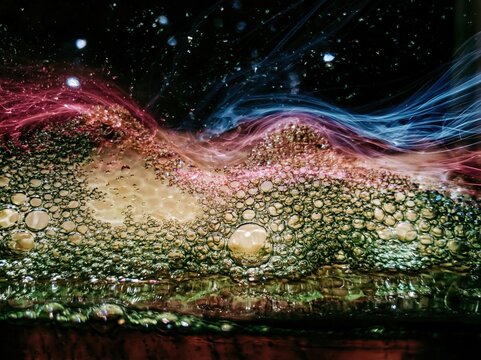 Green viscous liquid texture with air bubbles and colored light ribbons on a dark background for organic food branding, skincare packaging and meditative abstract art