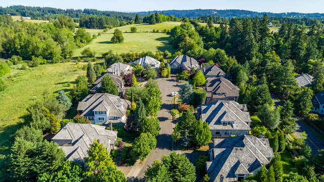 Aerial view of suburban houses with grey roofs nestled among lush green trees and grassy fields in a residential neighborhood in Lake Oswego, Oregon, United States.