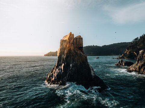 Aerial view of a prominent sea stack rising from the Pacific Ocean near the rugged coastline of Cannon Beach, Oregon, United States.