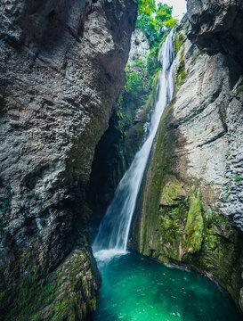 Aerial view of Chute de la Druise cascading down a narrow rocky gorge into a turquoise pool surrounded by mossy cliffs and lush greenery in Plan-de-Baix, Auvergne-Rhone-Alpes, France.