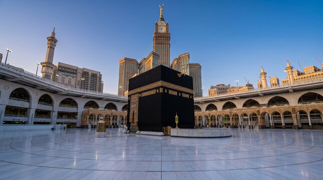 Wide-angle view of the Holy Kaaba in Masjid al-Haram, Mecca, under a clear blue sky, with the iconic Makkah Royal Clock Tower standing tall in the background.