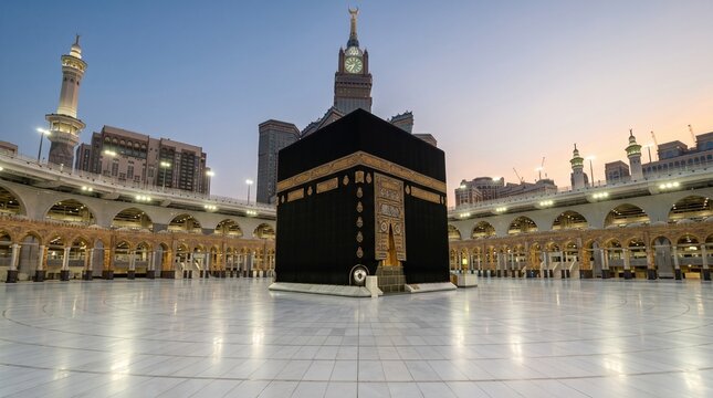 Beautiful evening twilight view of the Holy Kaaba in Mecca, showing the grand marble courtyard and illuminated arches with the Makkah Royal Clock Tower in the background.