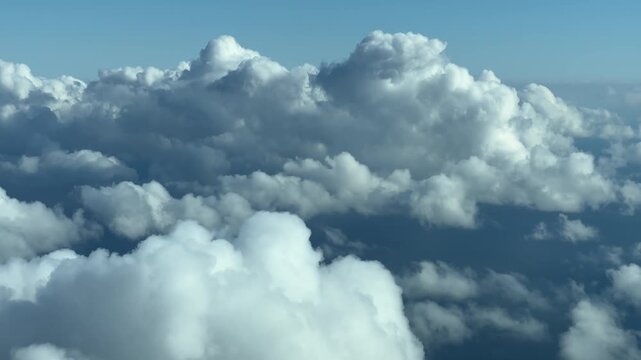 Looking down on fluffy white clouds from airplane window during daytime flight.