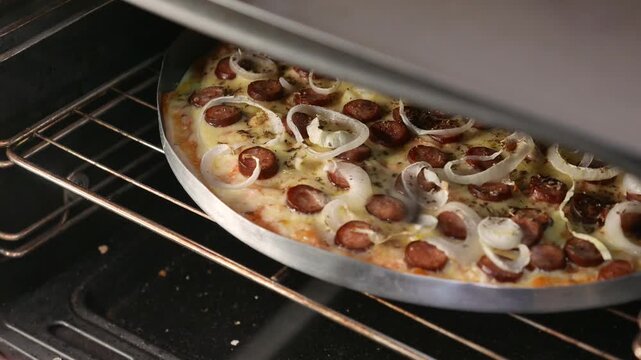 POV (slowly zooming out): pizza maker checking the pizza inside the oven. Chef rotates the pizza with a spoon. Close-up: Pepperoni, mozzarella, and onion pizza baking in the oven. Making pizza. 