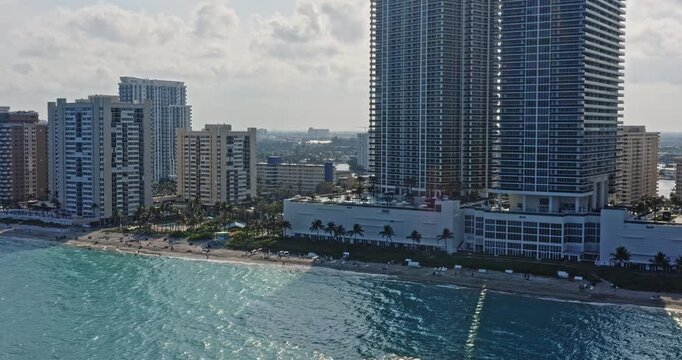 Hallandale Beach Florida Aerial v7 drone shot capturing luxurious beachfront condo towers and beach goers sunbathing on the shore on a tranquil sunny day - March 2021