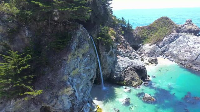 Stunning aerial footage of Mcway falls cascading onto sandy beach cove.