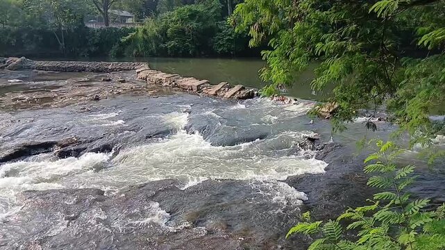 High angle shot of river water cascading over a small rocky dam structure creating white foam and rapids
