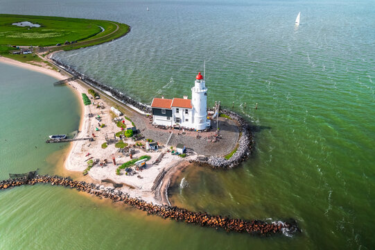 Aerial view of the historic Marken Lighthouse on a peninsula surrounded by the Markermeer, with a stone breakwater and green coastline in Marken, North Holland, Netherlands.