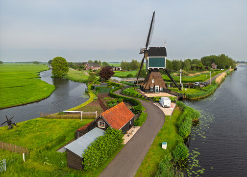 Aerial view of a traditional Dutch windmill situated along a winding canal in the lush green countryside of Groot-Ammers, South Holland, Netherlands.